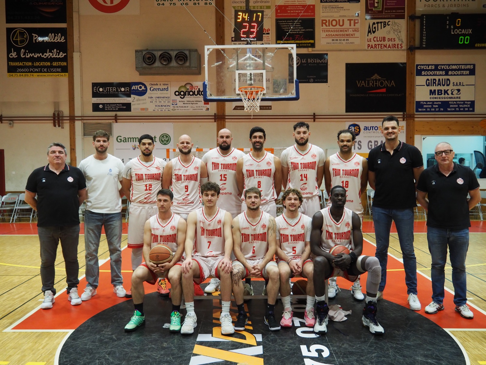 L'équipe de basket Twin Tournon posant sur le terrain avec leurs entraîneurs sous le panier.