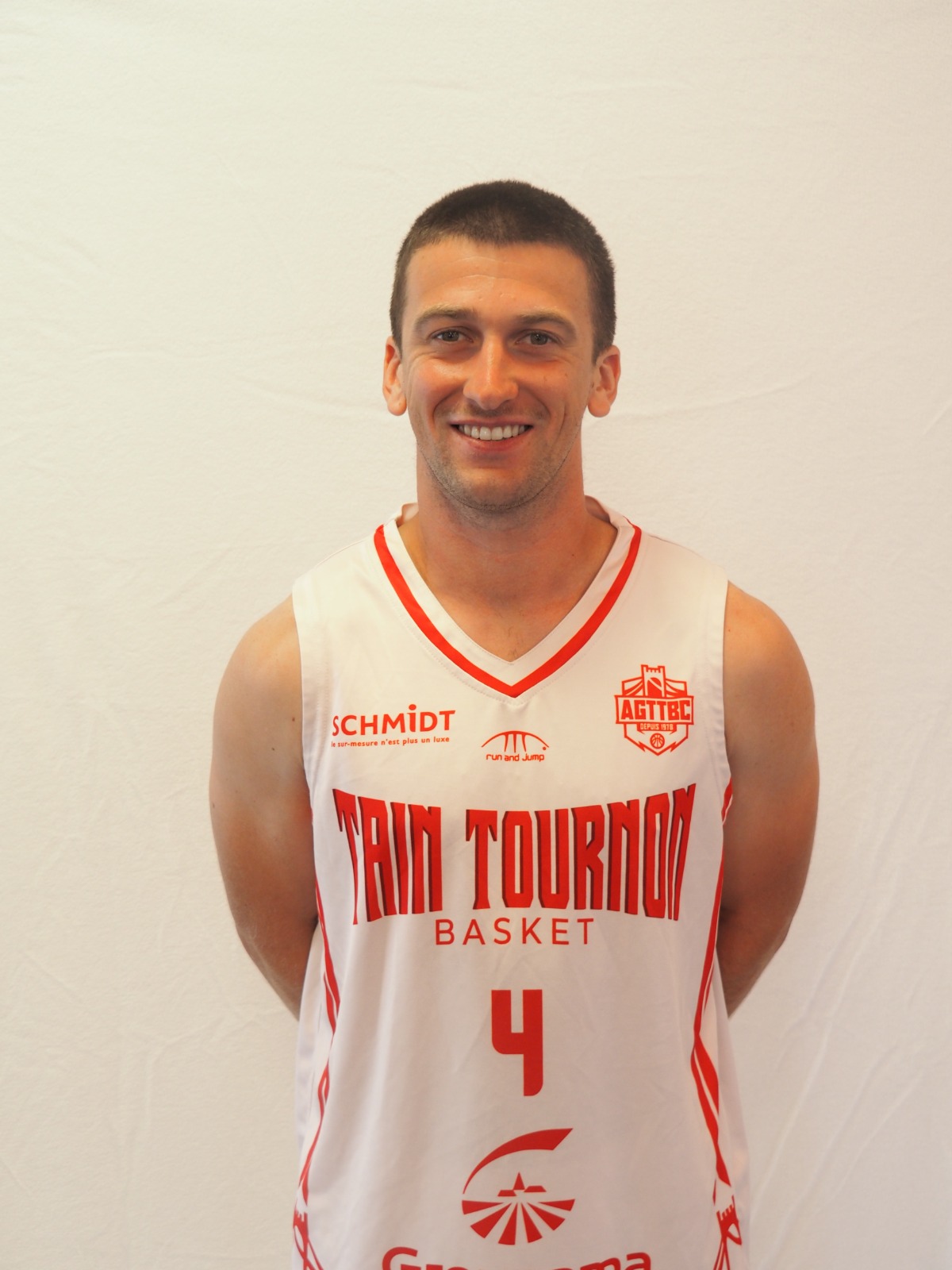 Homme souriant portant un maillot de basket blanc et rouge avec le numéro 4, sur fond blanc.