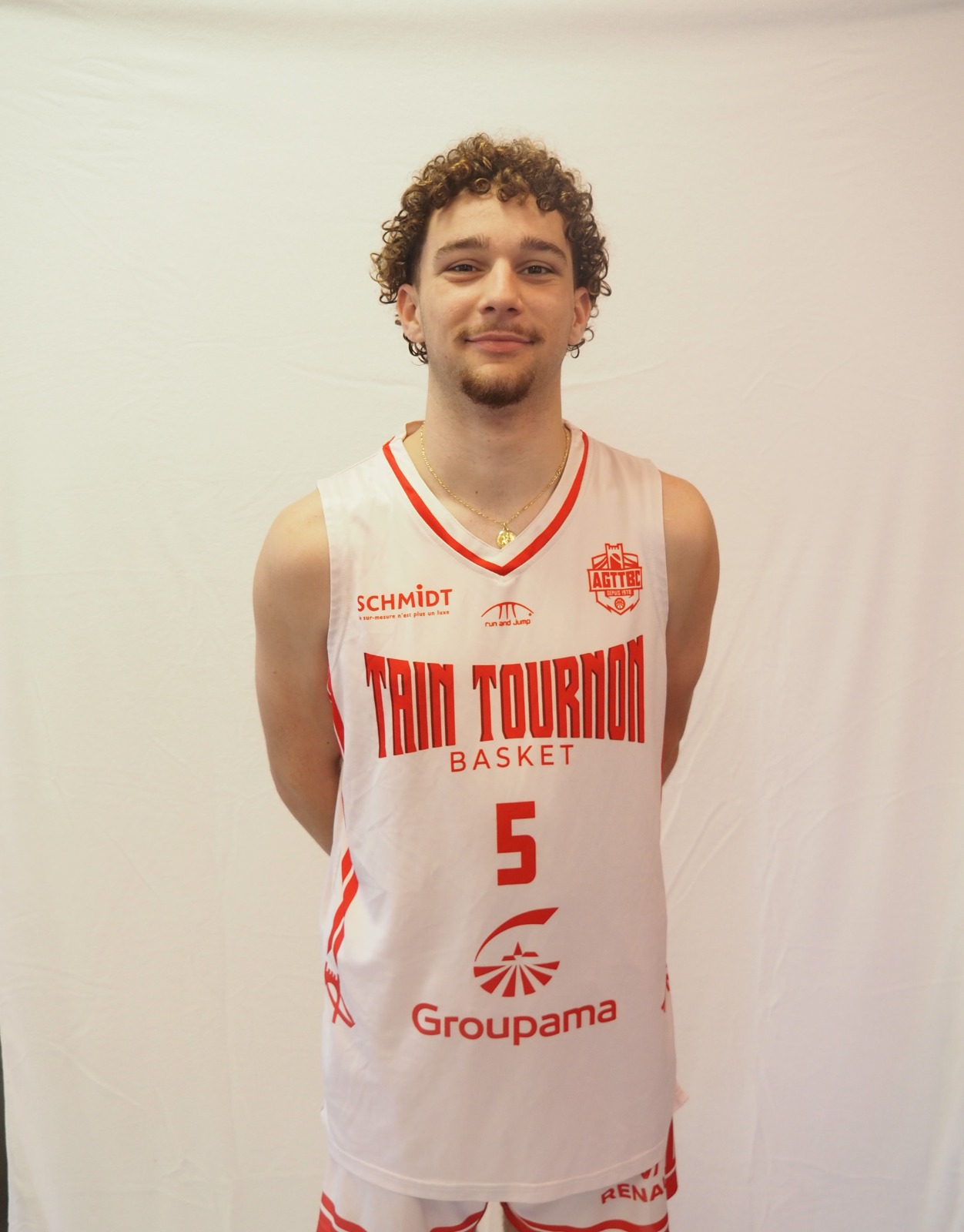 Jeune joueur de basket avec maillot blanc Tain Tournon numéro 5, logos de sponsors visibles.