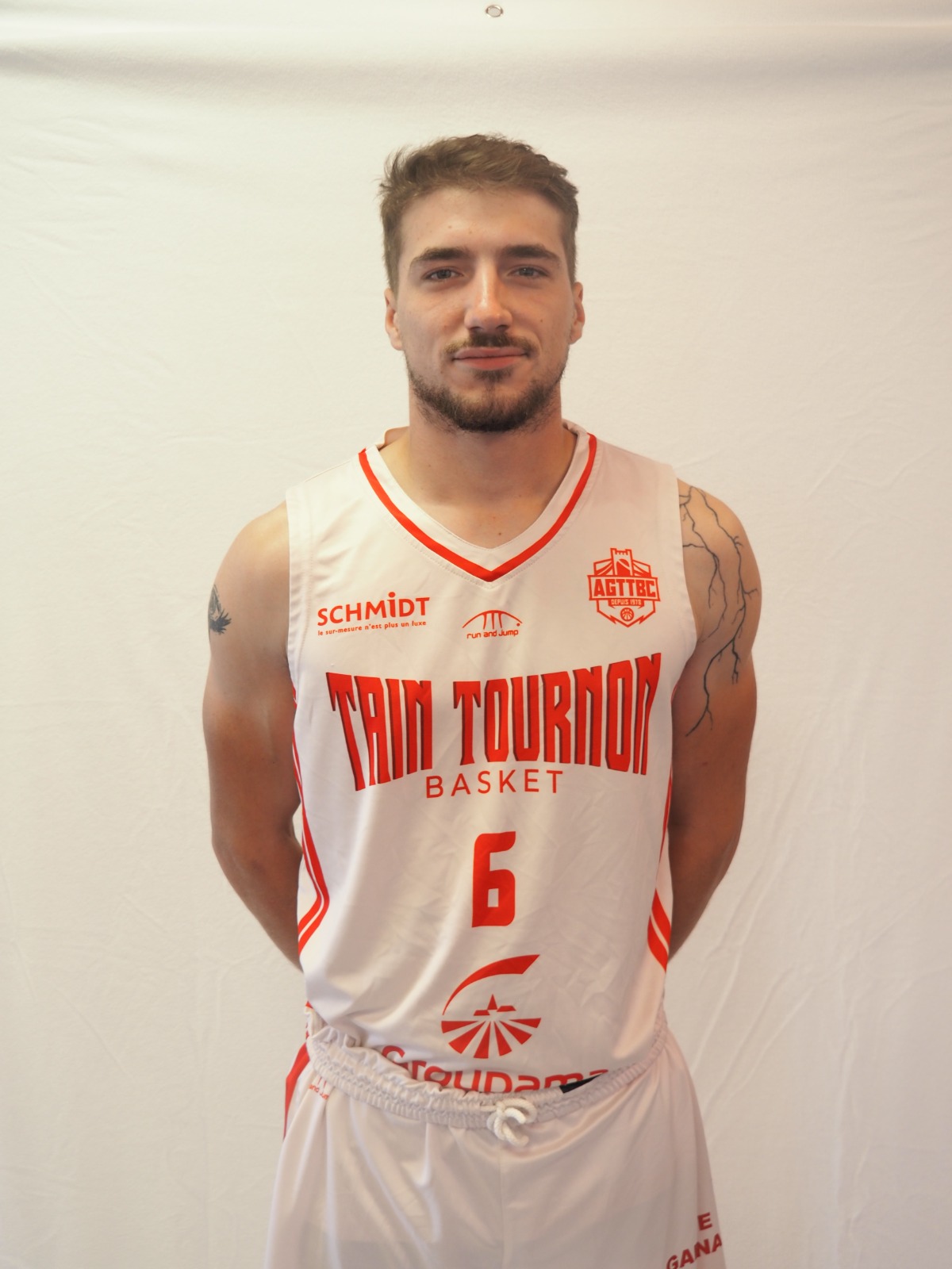 Joueur de basket en maillot blanc de l'équipe Tain Tournon, numéro 6, avec tatouages aux bras.