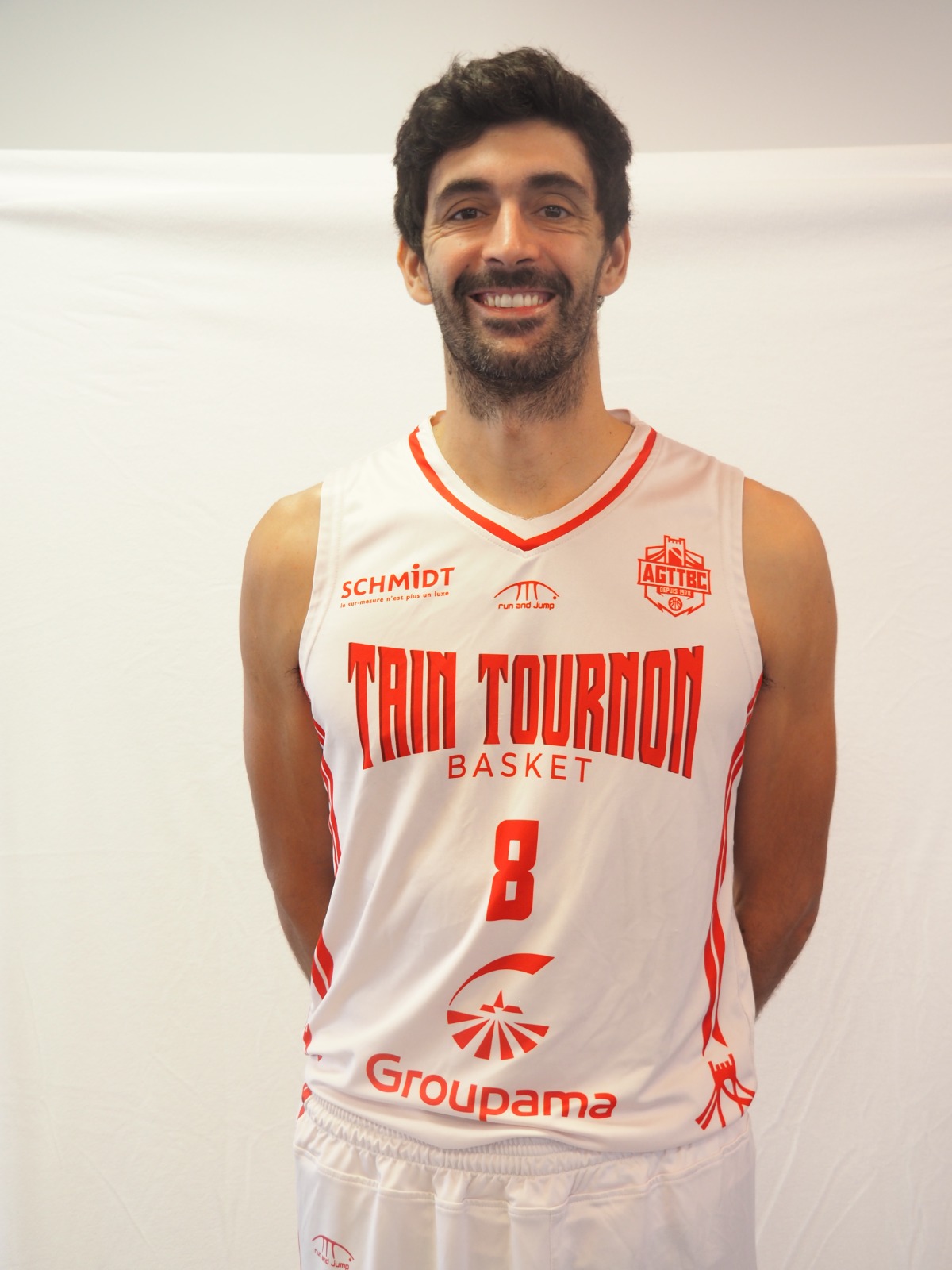 Joueur de basket souriant en maillot blanc et rouge de Tain Tournon Basket numéro 8.