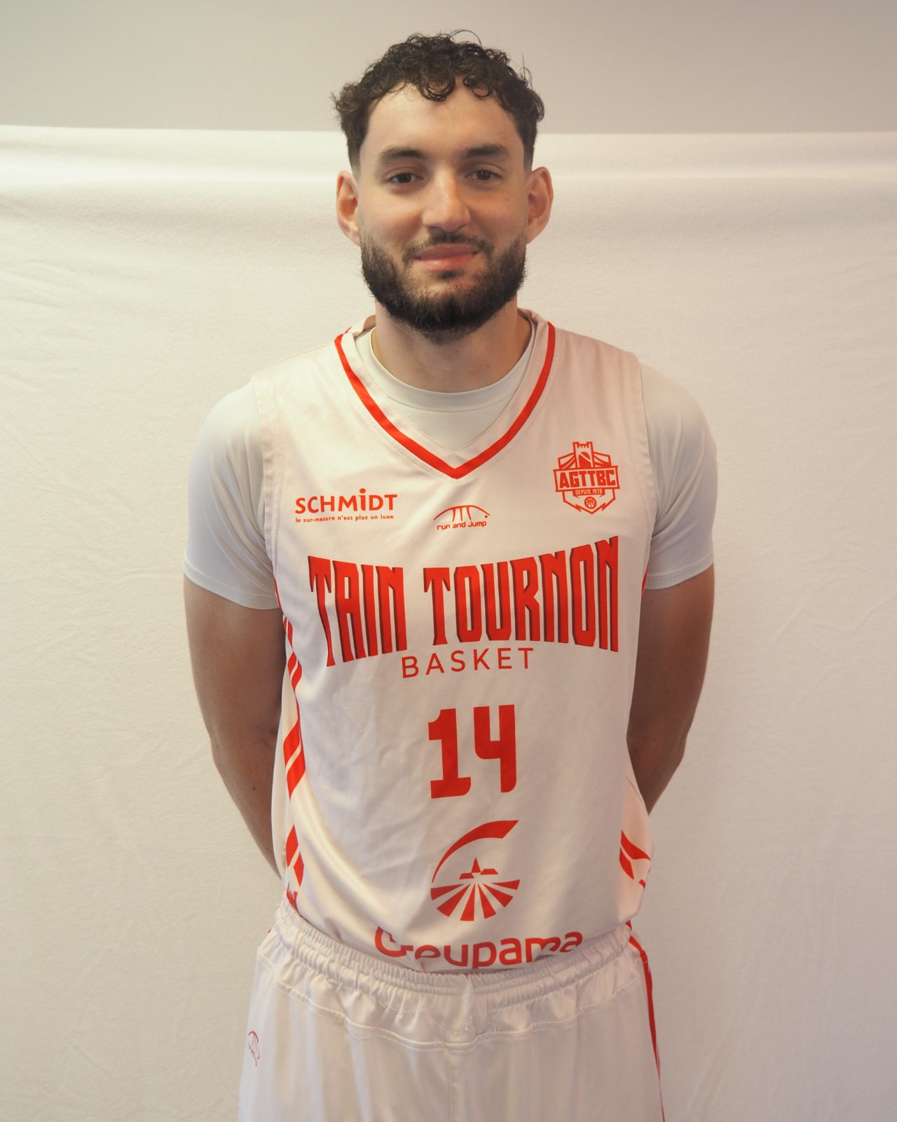 Joueur de basketball souriant en maillot blanc et rouge numéro 14 de Tain Tournon Basket.