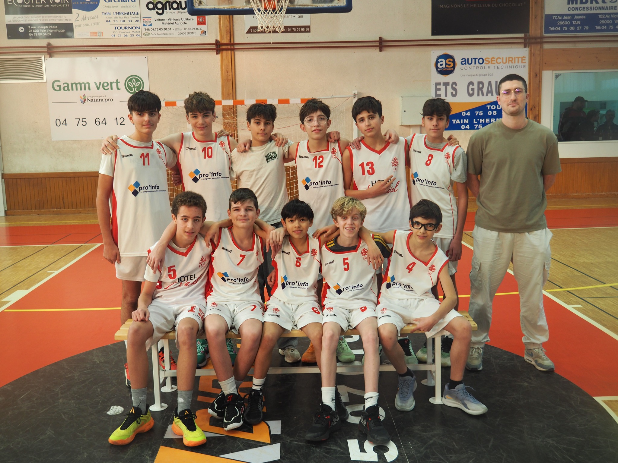 Equipe masculine de basket-ball de jeunes portant des uniformes blancs et rouges en gymnase.