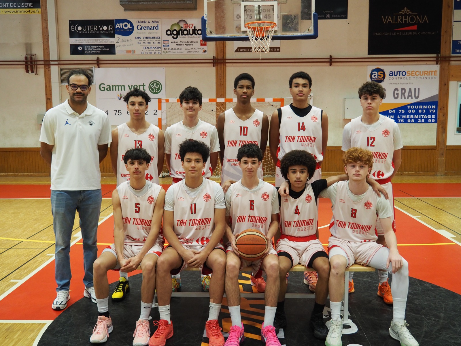 Une équipe de basketball des jeunes en maillots blancs posant avec leur entraîneur dans un gymnase.