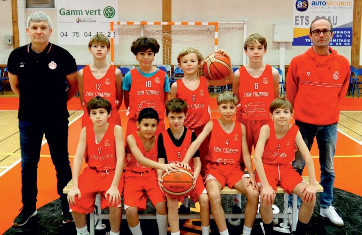 Équipe de basketball junior en maillots rouges posant avec deux entraîneurs dans un gymnase.