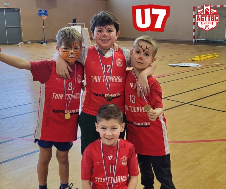 Quatre jeunes garçons en maillots rouges avec médailles, maquillés, dans un gymnase.