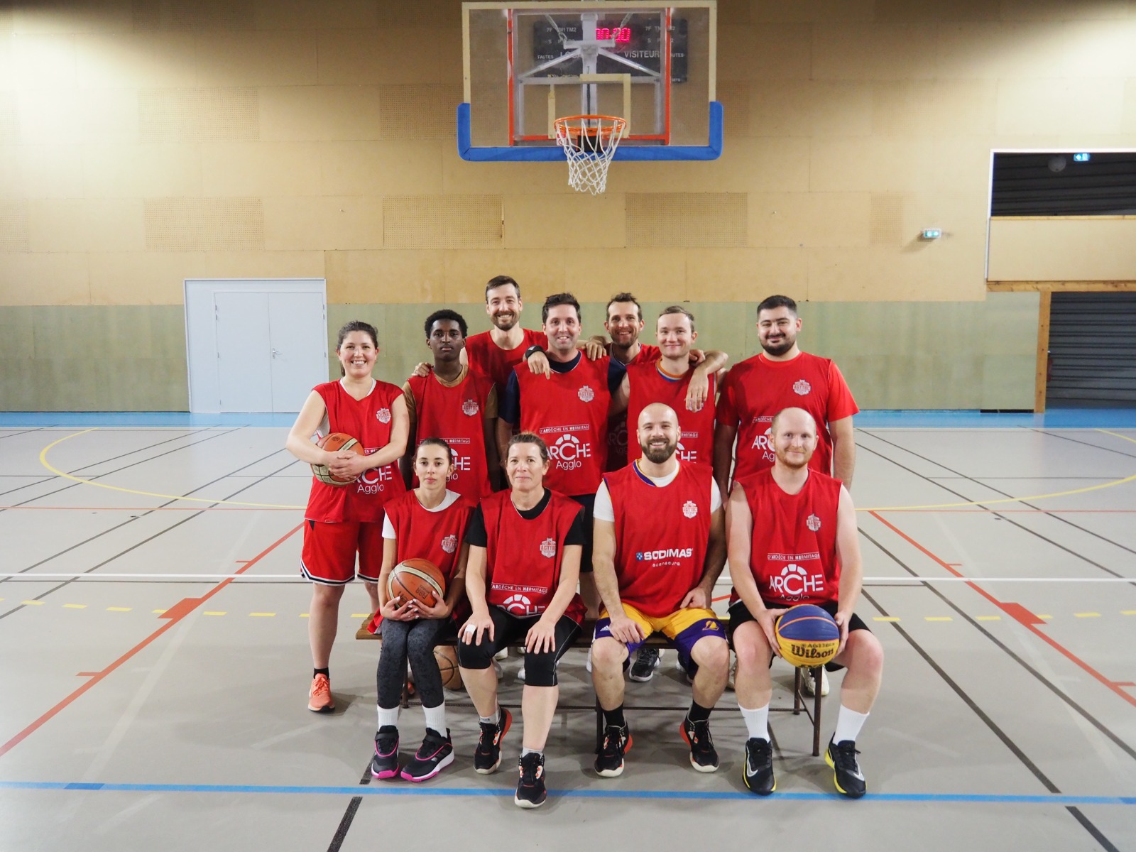 Une équipe de basket mixte en maillots rouges posant dans un gymnase sous un panier.