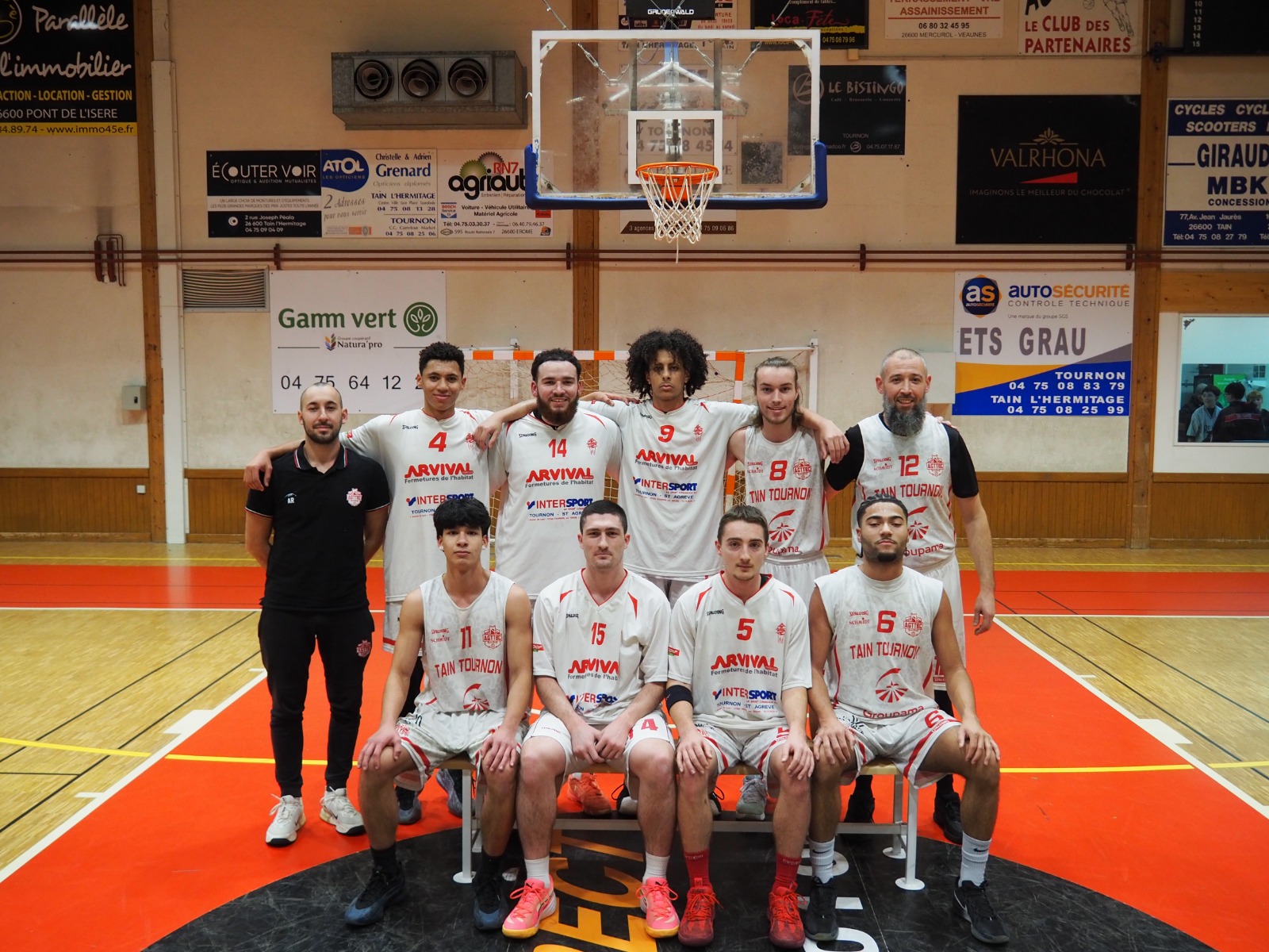 Équipe de basketball posant dans un gymnase avec leurs maillots blancs numérotés.