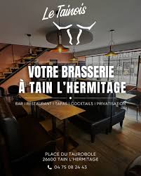 Intérieur moderne d'une brasserie avec canapés noirs, grande fenêtre, escalier et lumière suspendue.