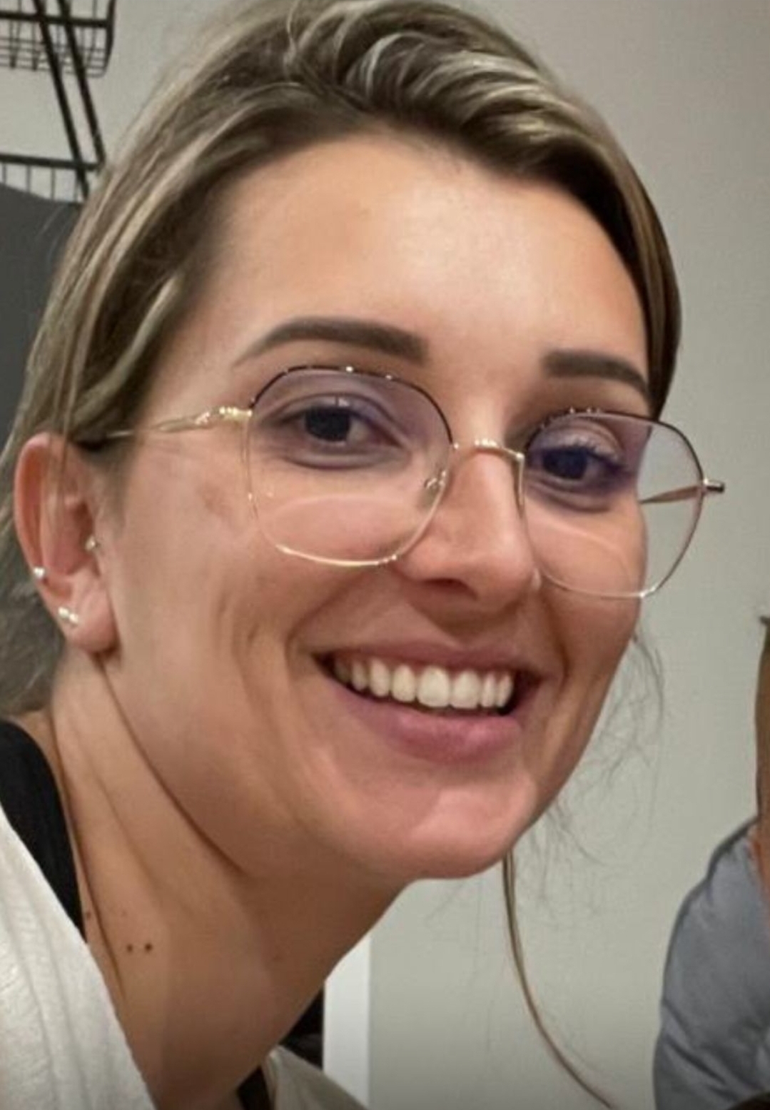 Portrait d'une femme souriante portant des lunettes à monture fine et cheveux blonds attachés.