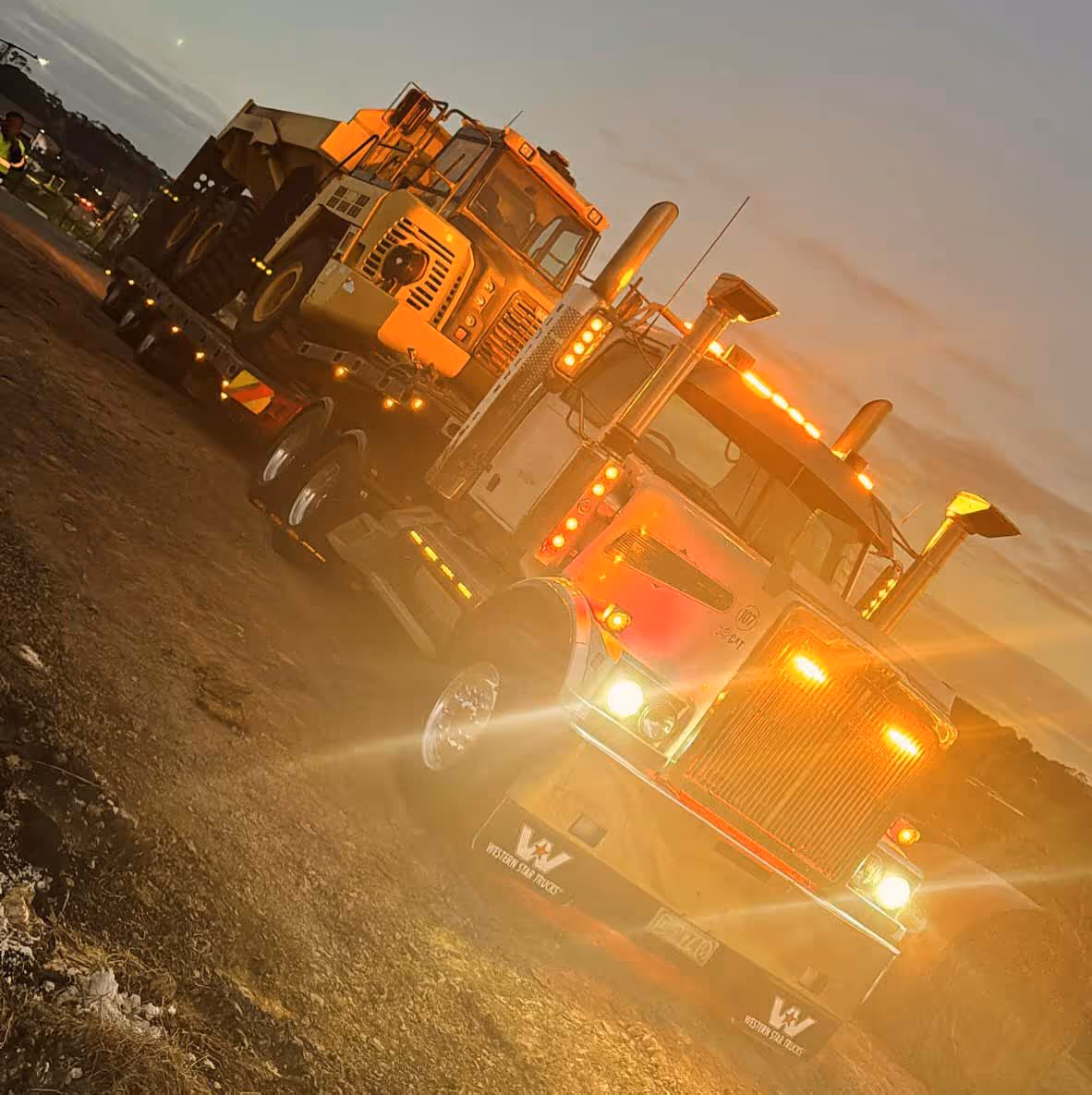 Western Star trucks hauling a second vehicle safely at sunset with headlights on.