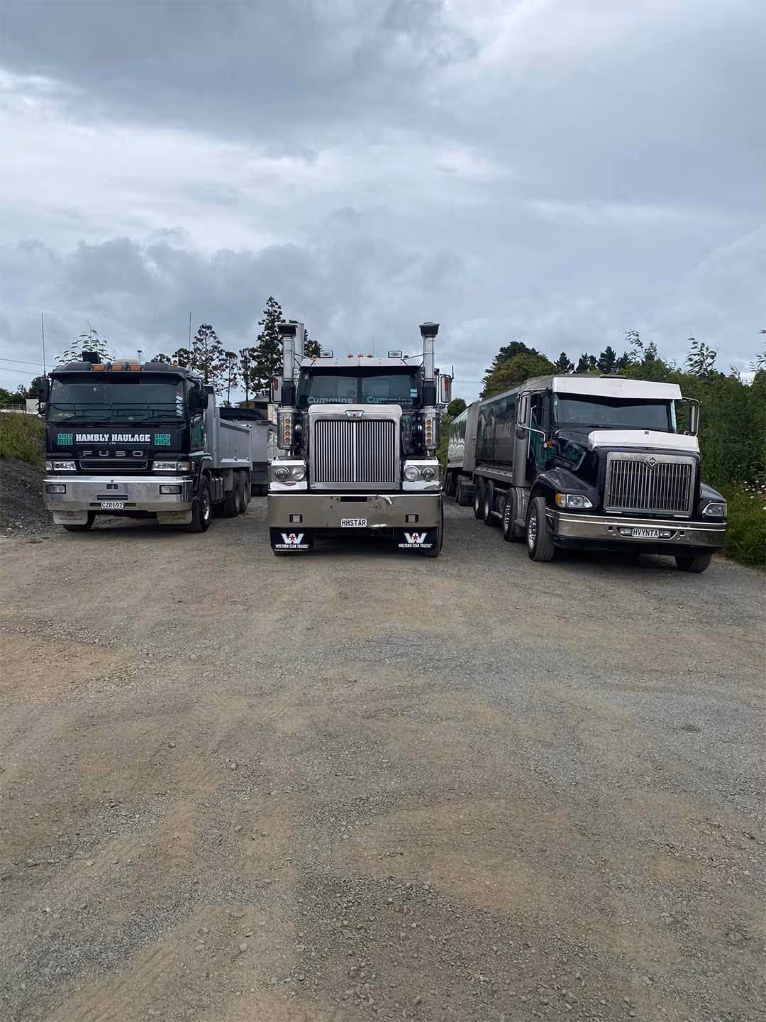 Large commercial Hambly Haulage trucks parked alongside Cummins engines on a rural gravel road.