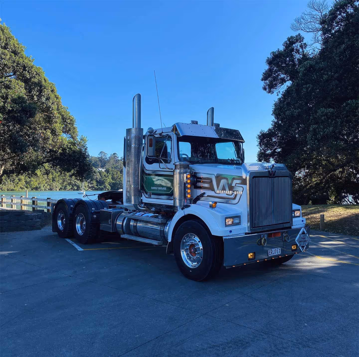 Western Star semi-truck parked on asphalt beside tranquil trees and serene natural water setting.