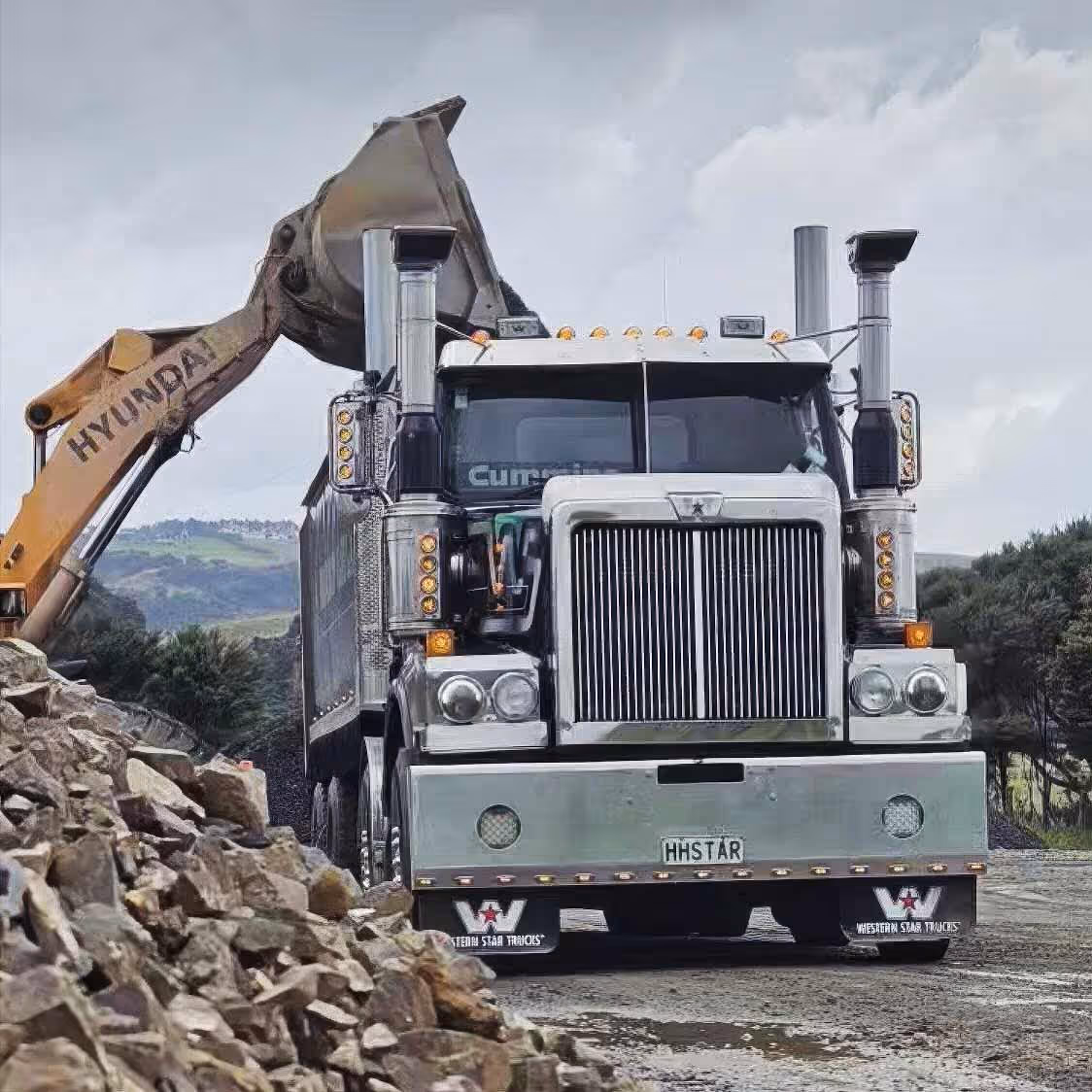 Western Star truck loads rocks with Hyundai excavator on a busy construction site.