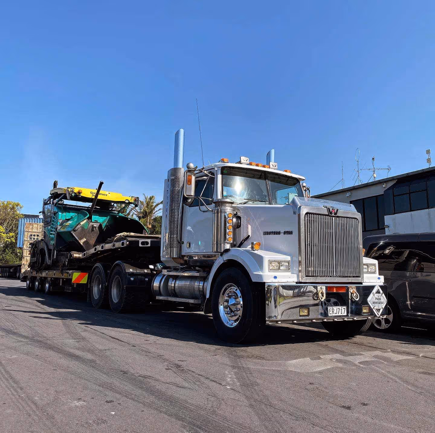 Western Star semi-truck hauling green and yellow construction equipment on a transport trailer.