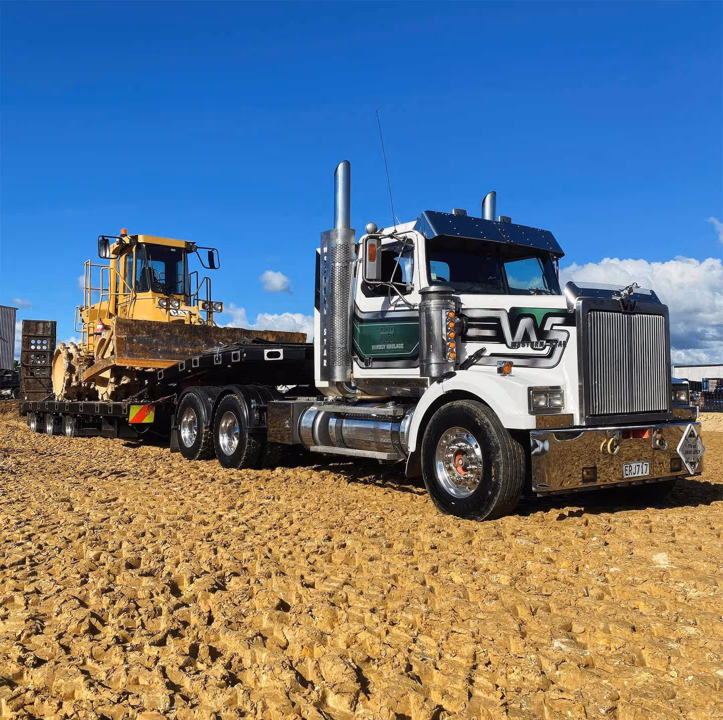 Heavy construction equipment transportation, Kenworth truck hauling Caterpillar bulldozer in a rural area.