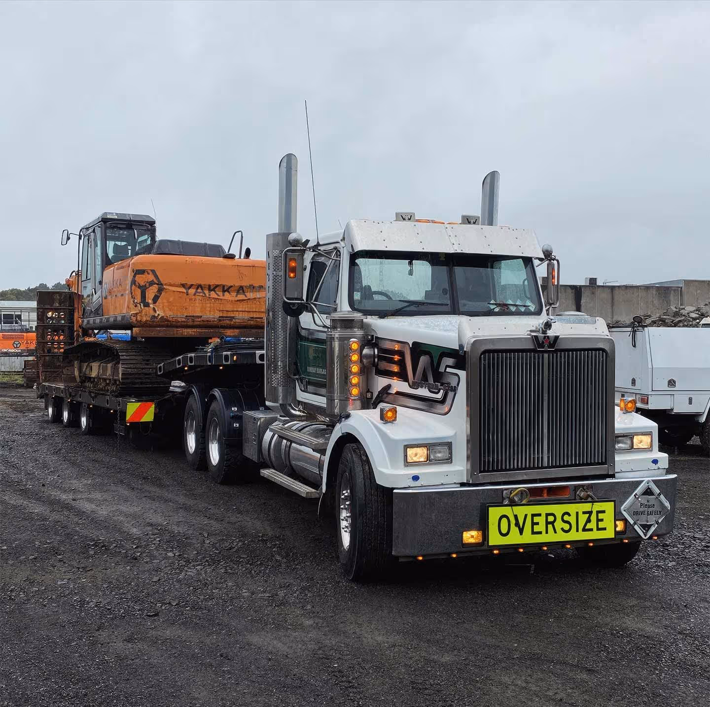 Oversized construction equipment being transported by large white semi-truck on a trailer securely.