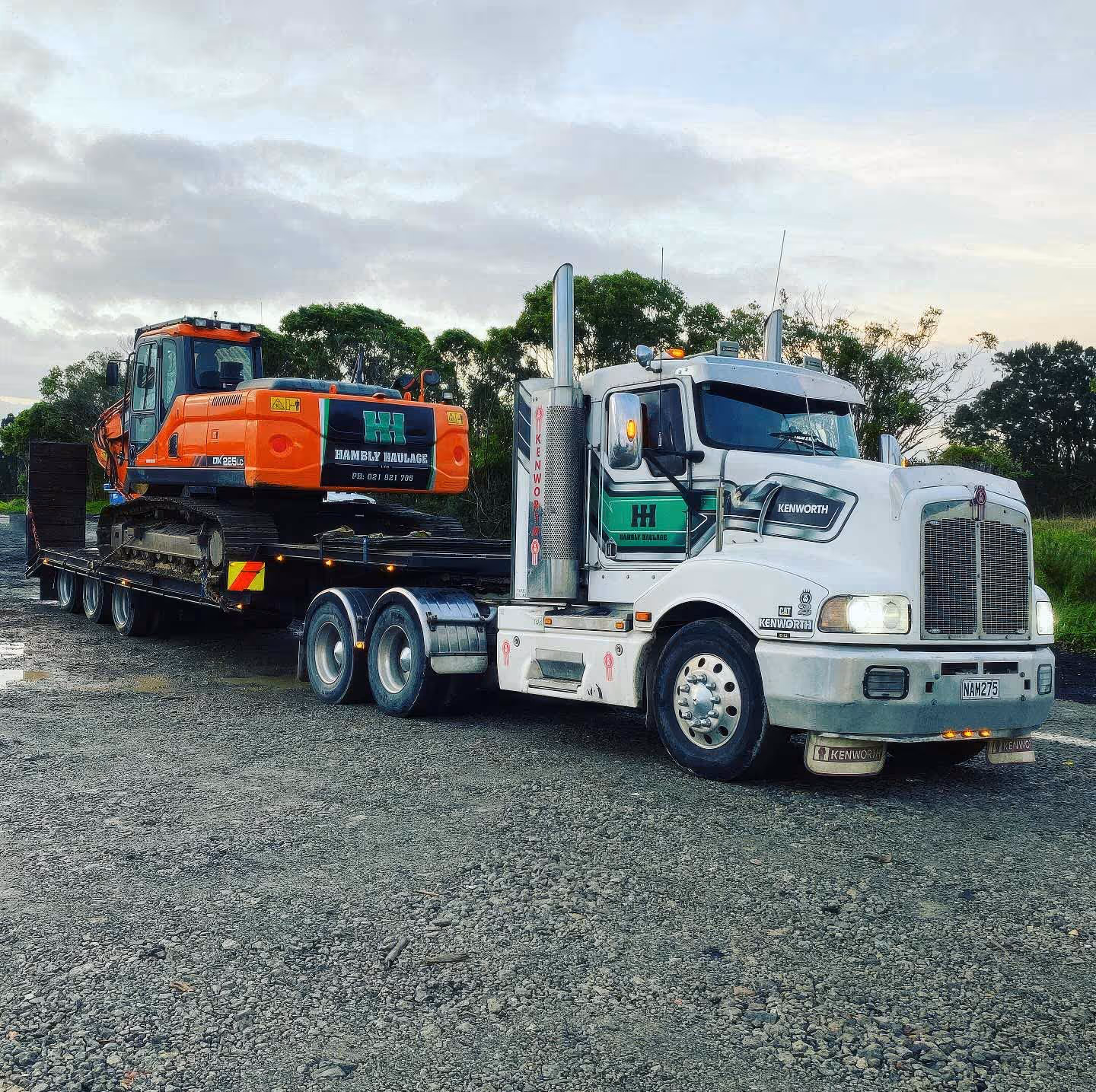 Large Kenworth truck hauling orange excavator with Hambly Haulage trailers for heavy industry transportation.