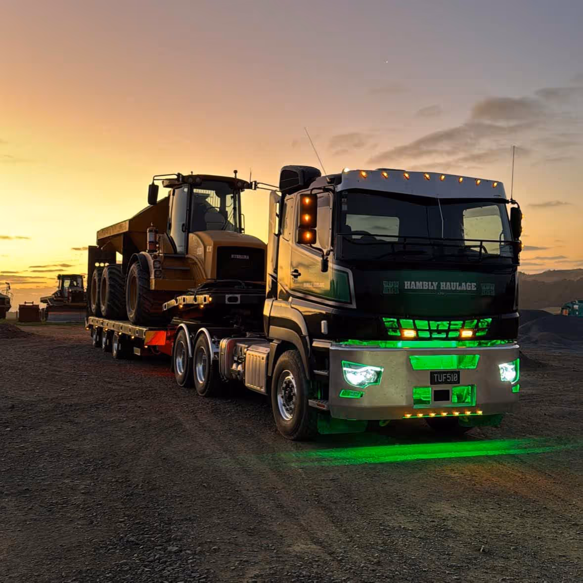 Green lights illuminate heavy equipment haulage truck hauling at a dramatic sunset backdrop.