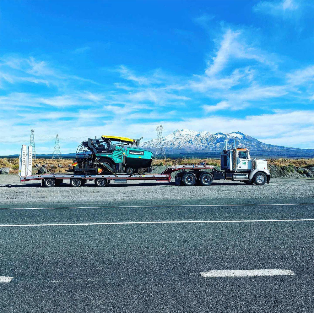 Heavy haulage truck transporting construction equipment on a trailer through Auckland terrain successfully. Hambly Haulage