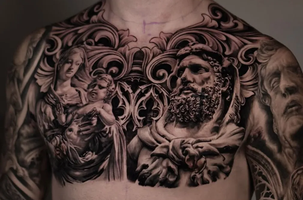 Close-up of a black and grey tattoo on the chest depicting classical sculptures of women and men with intricate background designs.