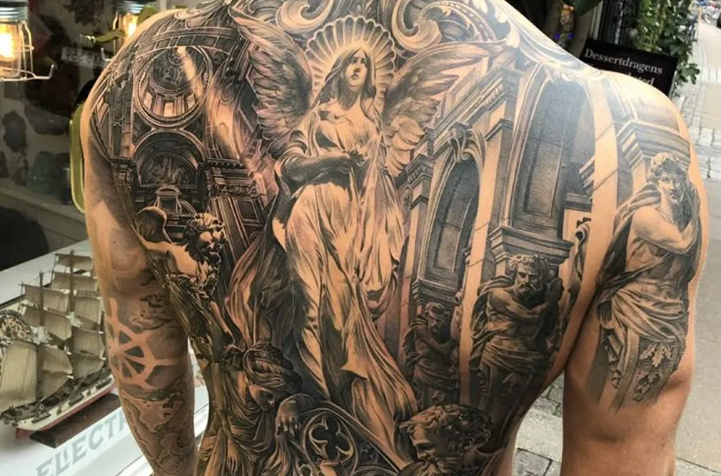 Detailed black and grey tattoo of a classical scene with Greek and Roman figures and ornate designs on the chest and back.