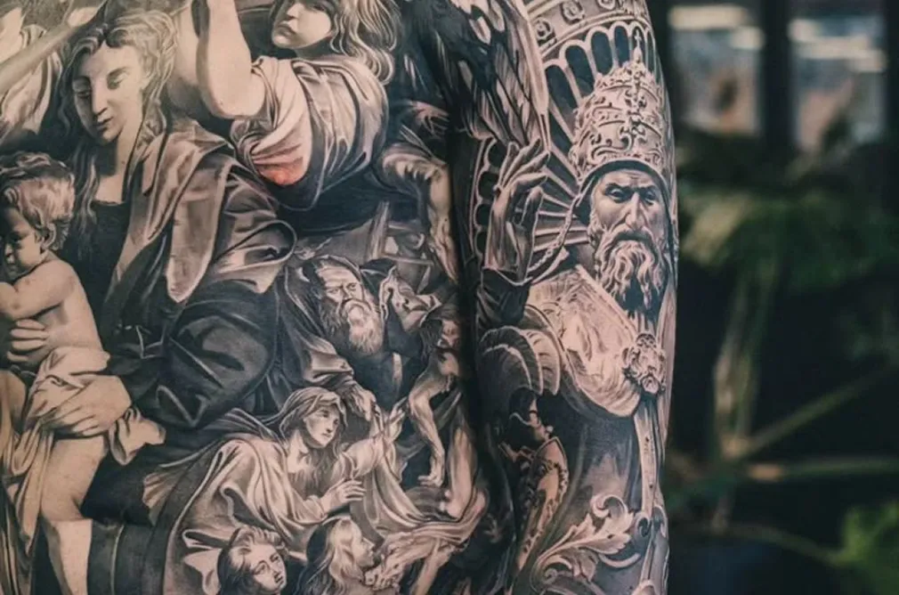 Black and grey tattoo depicting intricate classical figures and historical elements, covering the entire arm and chest.