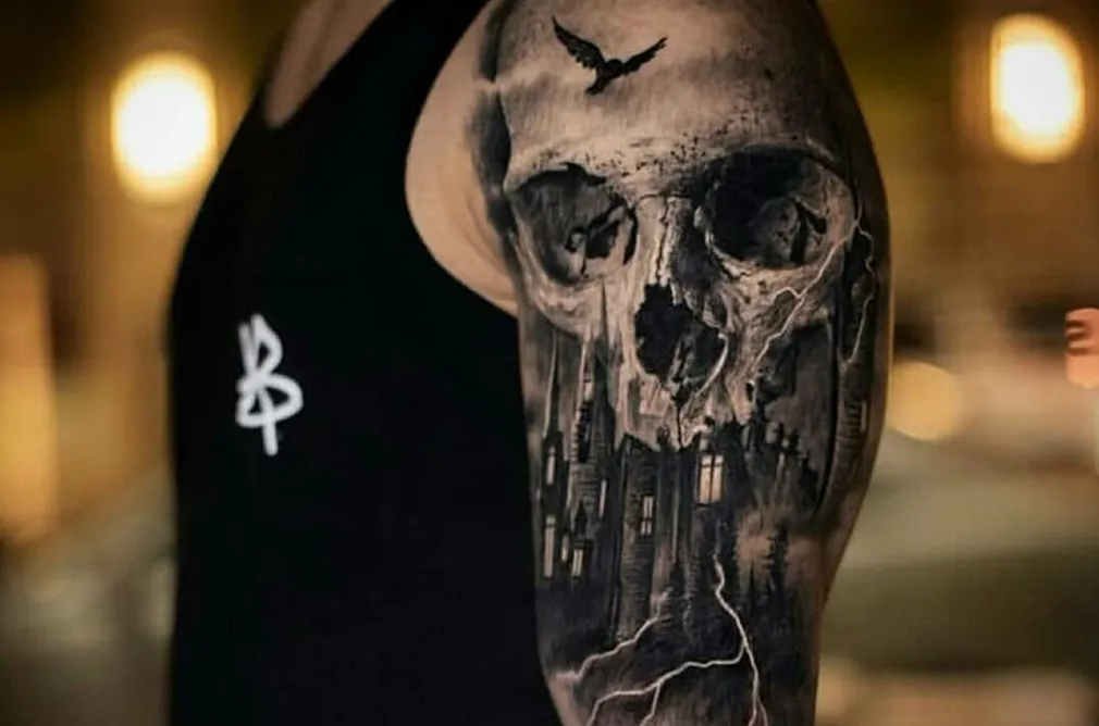 Tattoo of a skull with detailed shading, depicting gothic architecture and stormy elements on the arm.