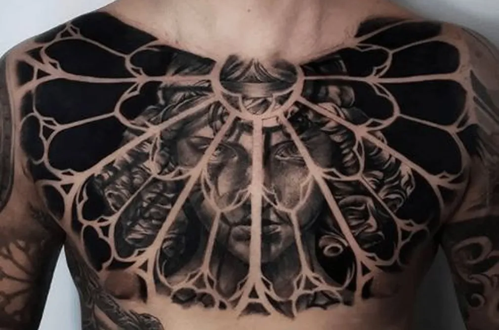 Bold black and grey tattoo of a woman’s face, featuring intricate designs and a symmetrical pattern radiating from the center.