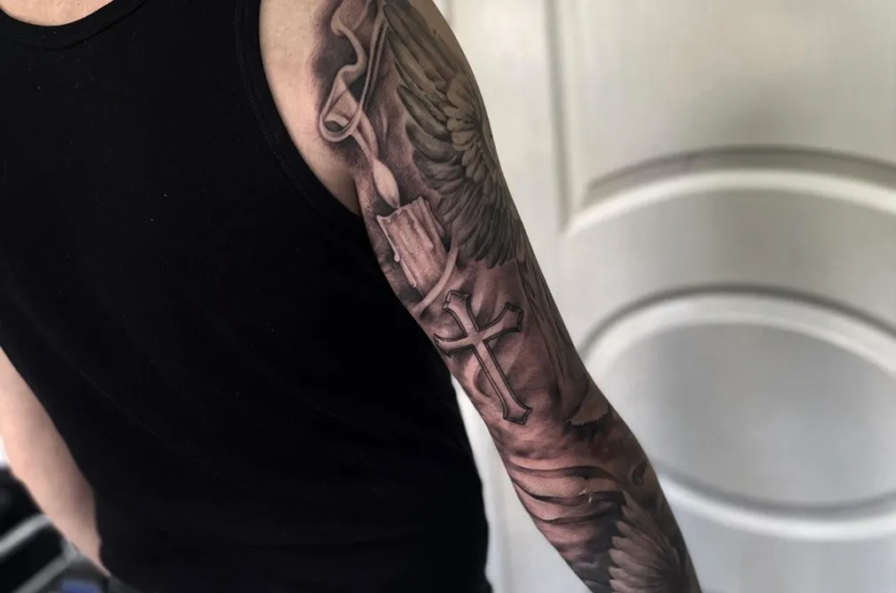 Black and grey tattoo of an angel with a sword and detailed wings, covering the entire arm with a heavenly and powerful theme.