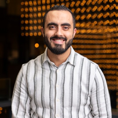 Lachende man met baard en gestreept wit-grijs overhemd voor een achtergrond met warme, vervaagde lichtjes.