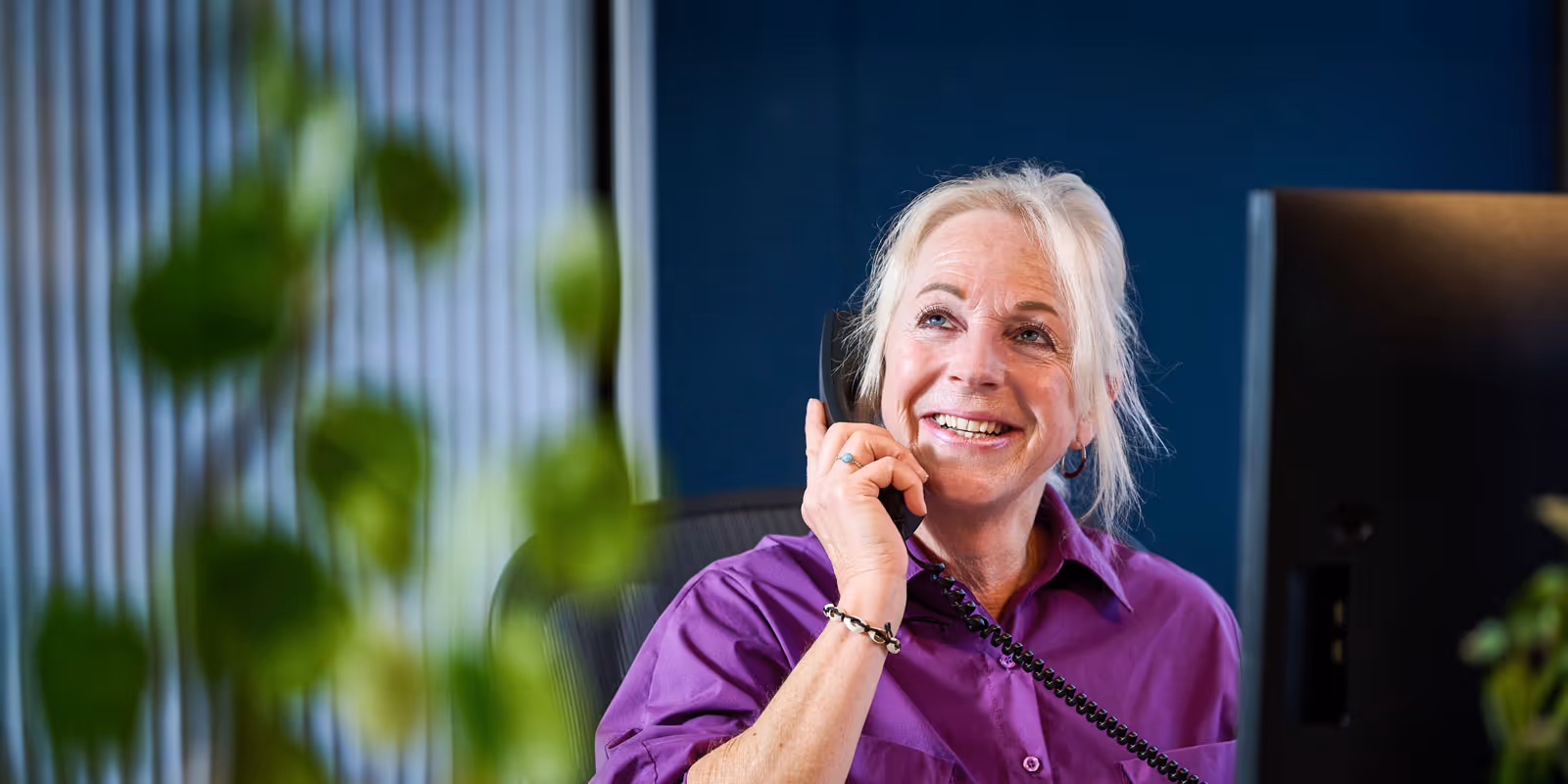 Vrolijke vrouw met een paarse blouse die aan de telefoon spreekt op kantoor.