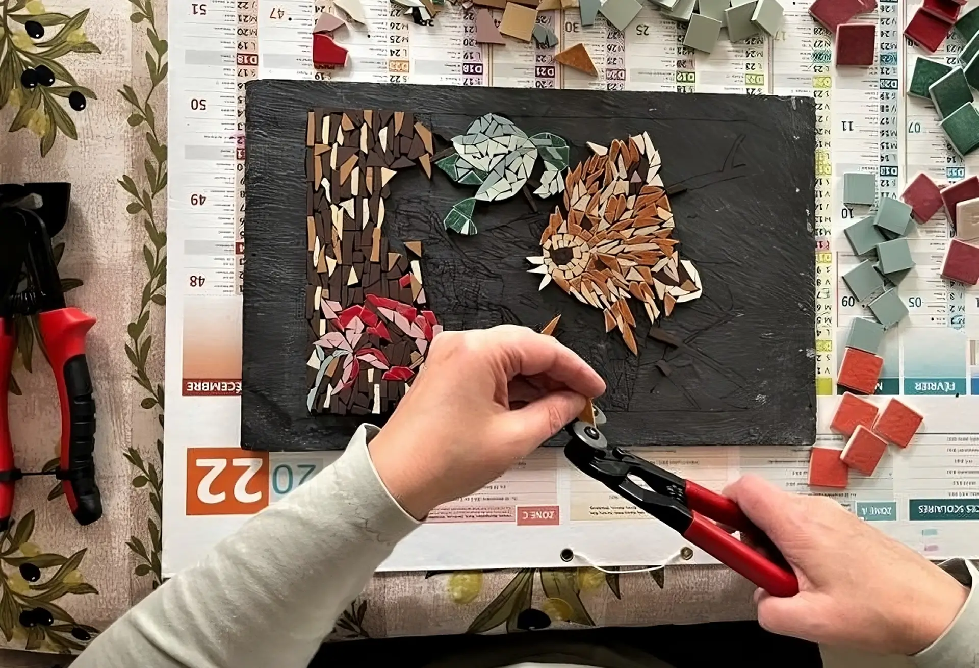 Mosaïque en cours de création représentant des poissons colorés, avec pièces et outils visibles autour de l'œuvre