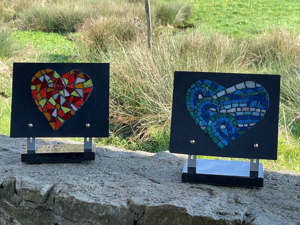 Deux plaques funéraires en forme de cœur, l'une rouge et l'autre bleue, posées côte à côte