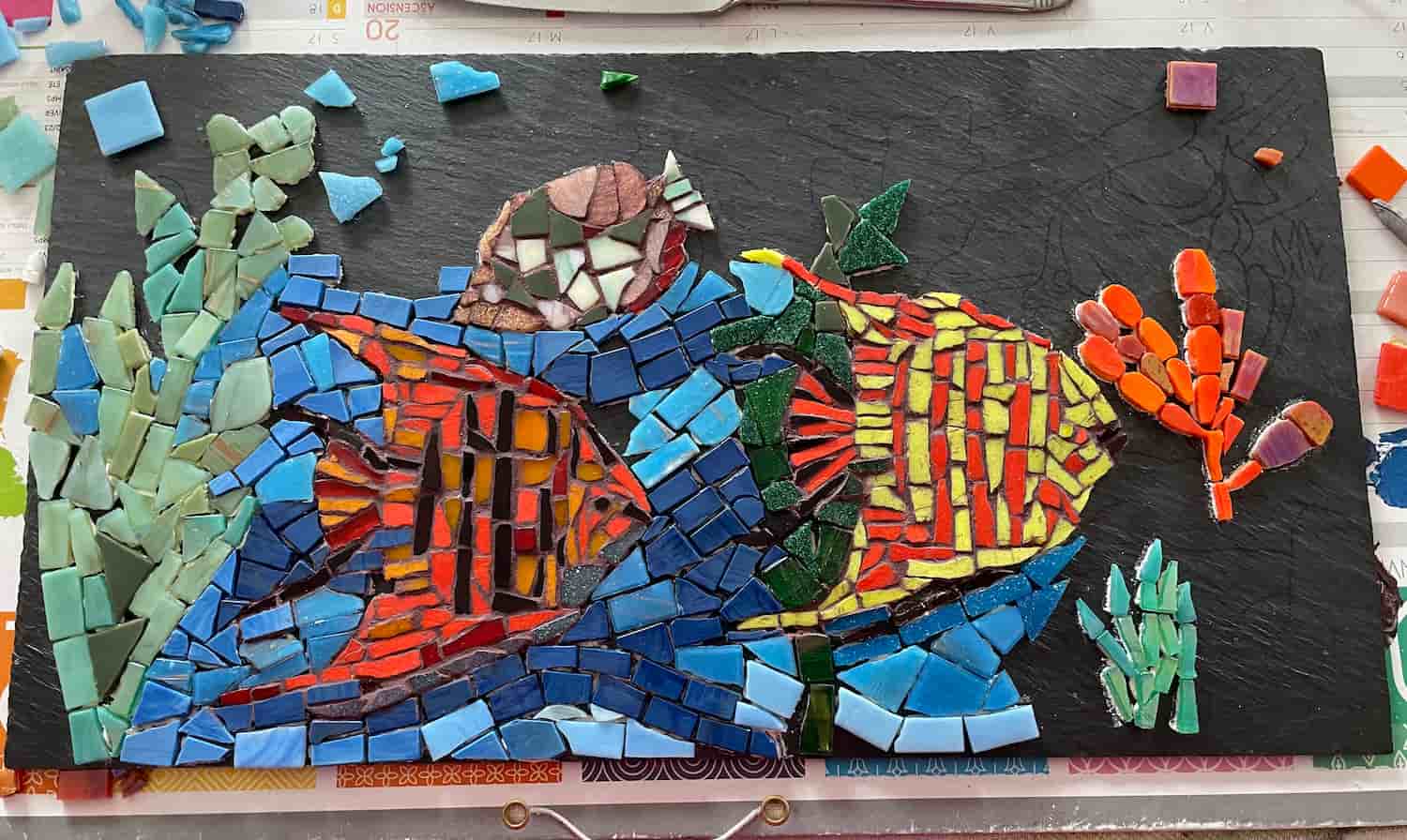 Mosaïque colorée représentant deux poissons tropicaux nageant parmi des plantes aquatiques sur un fond noir
