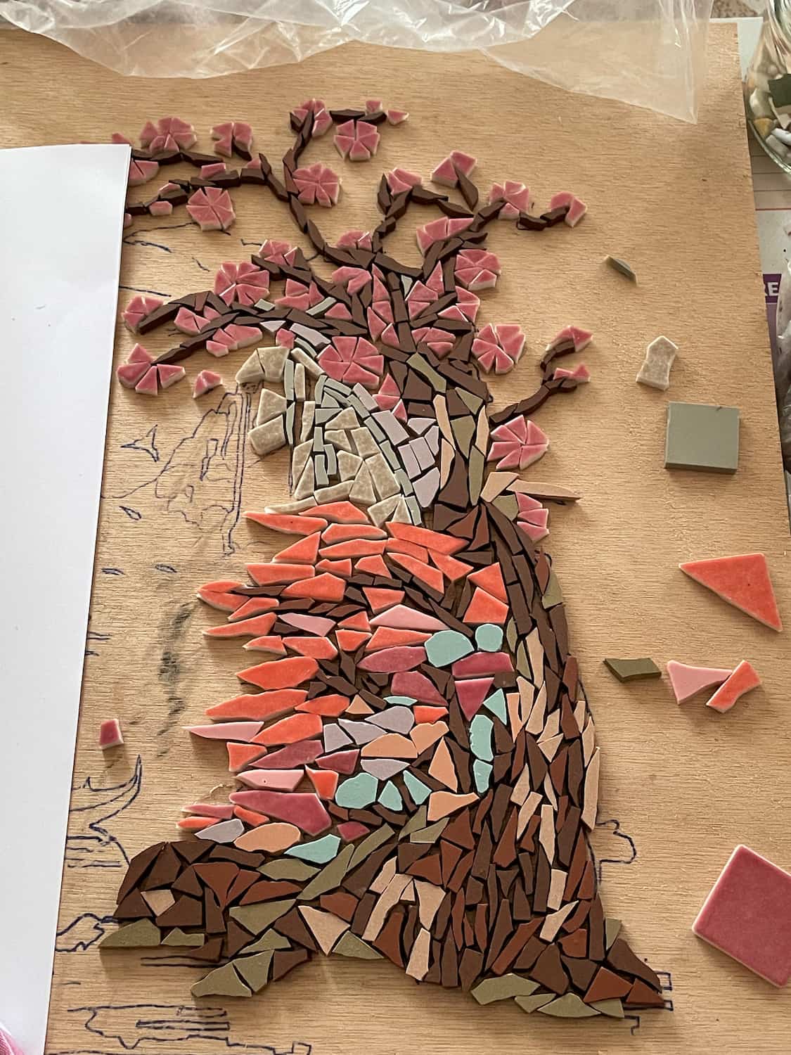 Mosaïque en cours de réalisation représentant un arbre en floraison avec des tesselles roses, rouges et brunes sur fond en bois