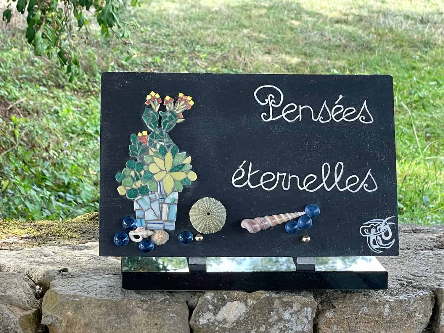 Plaque funéraire avec l'inscription "Pensées éternelles", entourée de fleurs dans un cimetière.