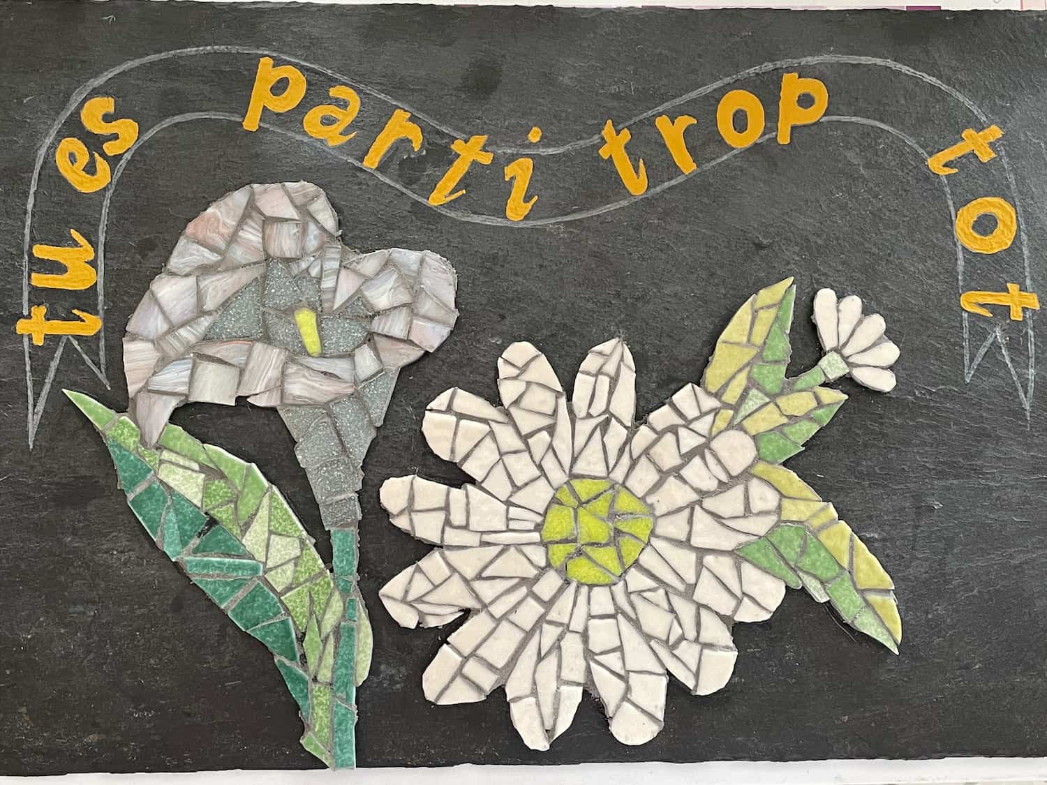 Plaque commémorative avec l'inscription 'Tu es parti trop tôt' et deux fleurs décoratives