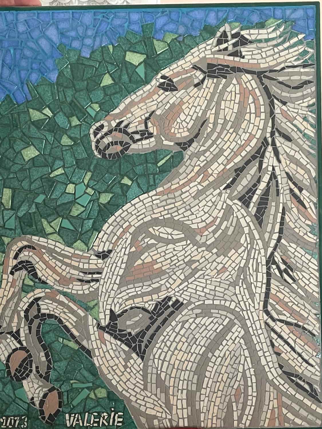 Mosaïque artistique représentant un cheval en mouvement, composée de tesselles colorées sur fond naturel