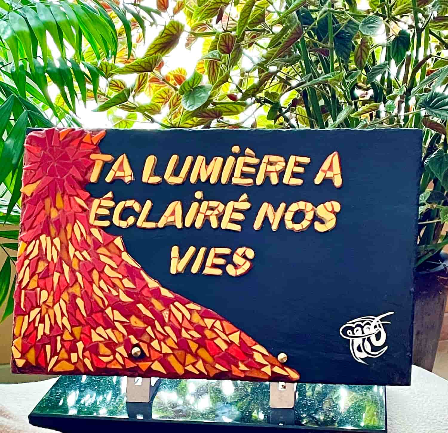 Plaque funéraire vue de face, avec l'inscription "ta lumière éclaire nos vies", ornée de décorations sobres et symboliques