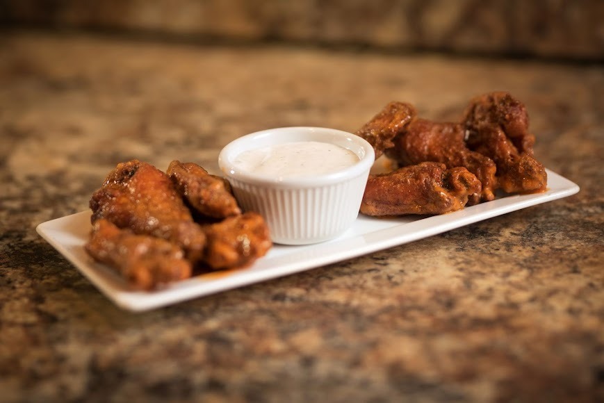 A plate featuring chicken wings accompanied by a small bowl of dipping sauce.
