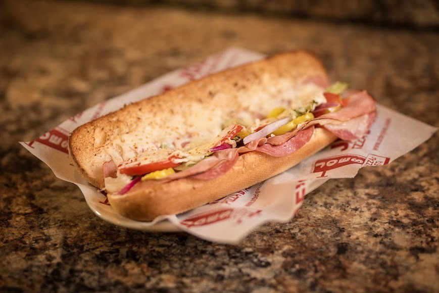 A sub sandwich filled with layers of meat, cheese, and fresh vegetables on a toasted hoagie roll.