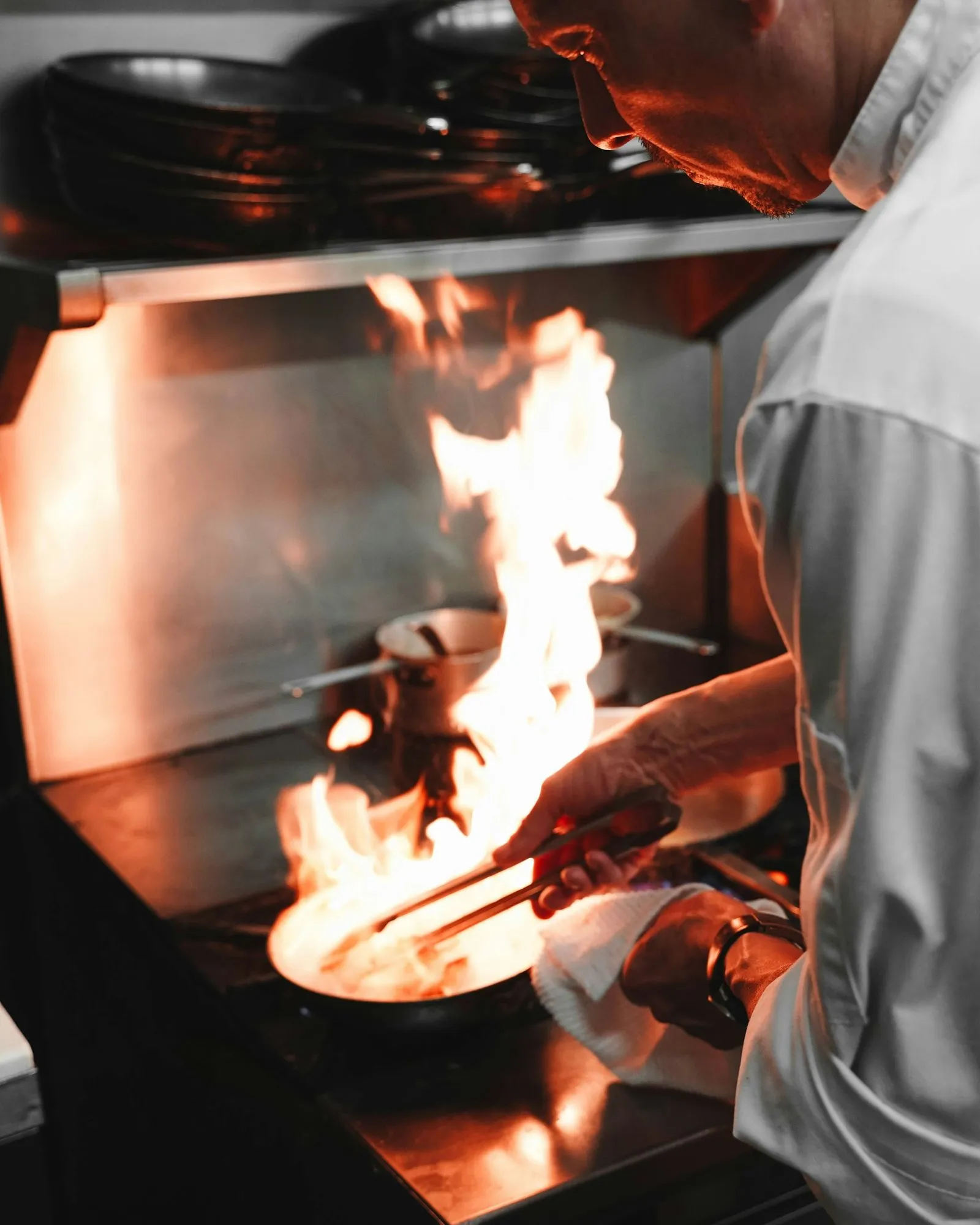 A chef is cooking on a grill with flames.