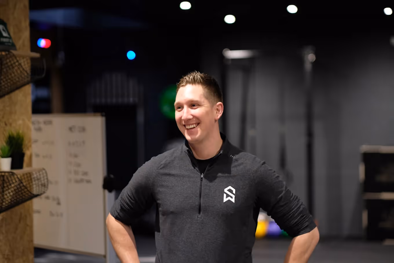 Man in a black polo shirt laughing in a gym