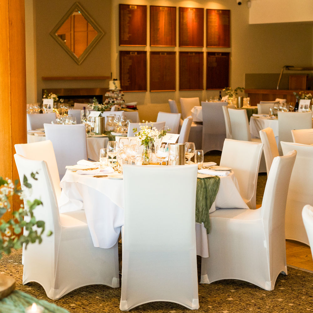A table and chair setup with white tablecloths for a wedding function in a golf club