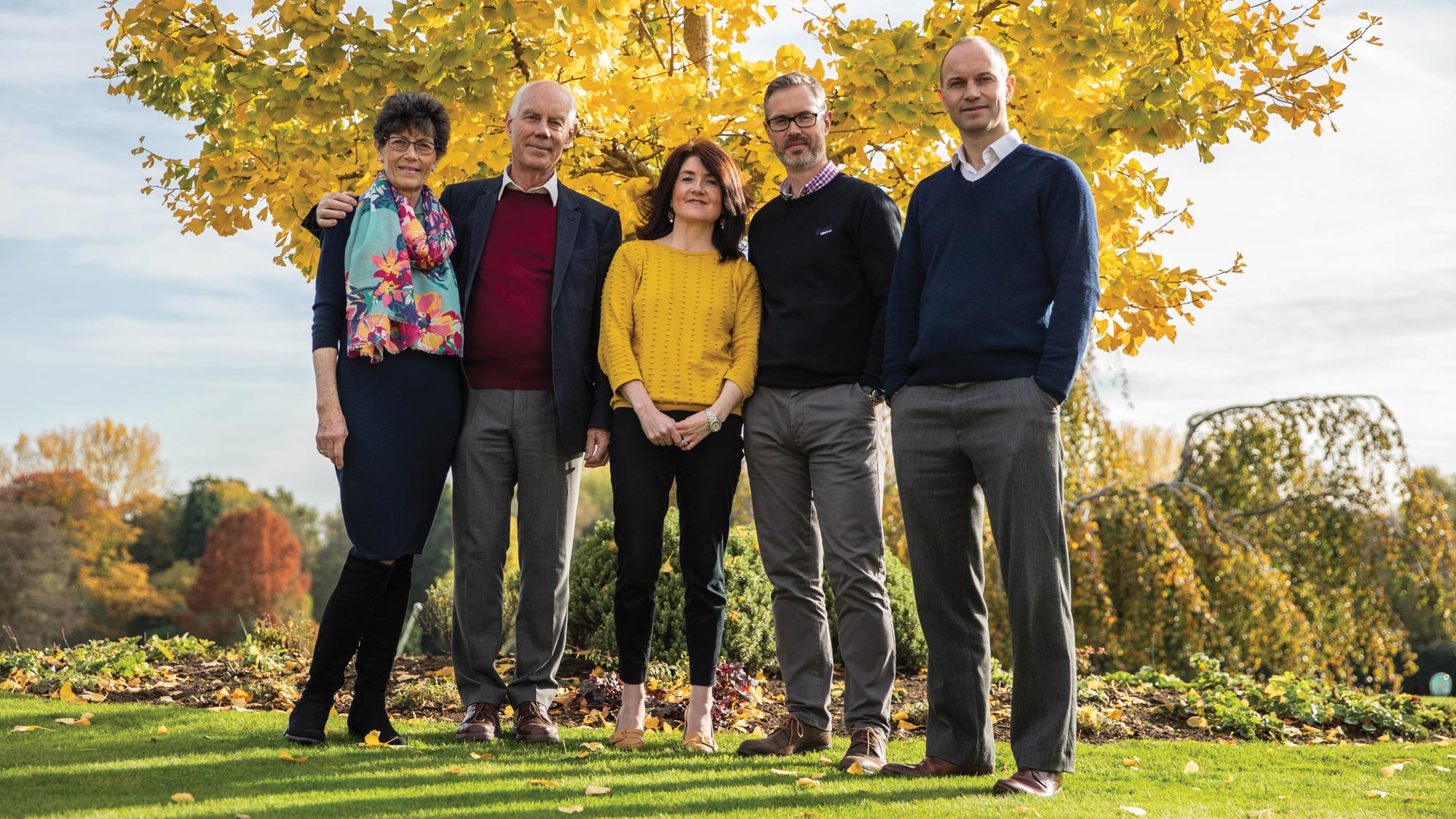 A family standing in front of a large tree in the autumn time.