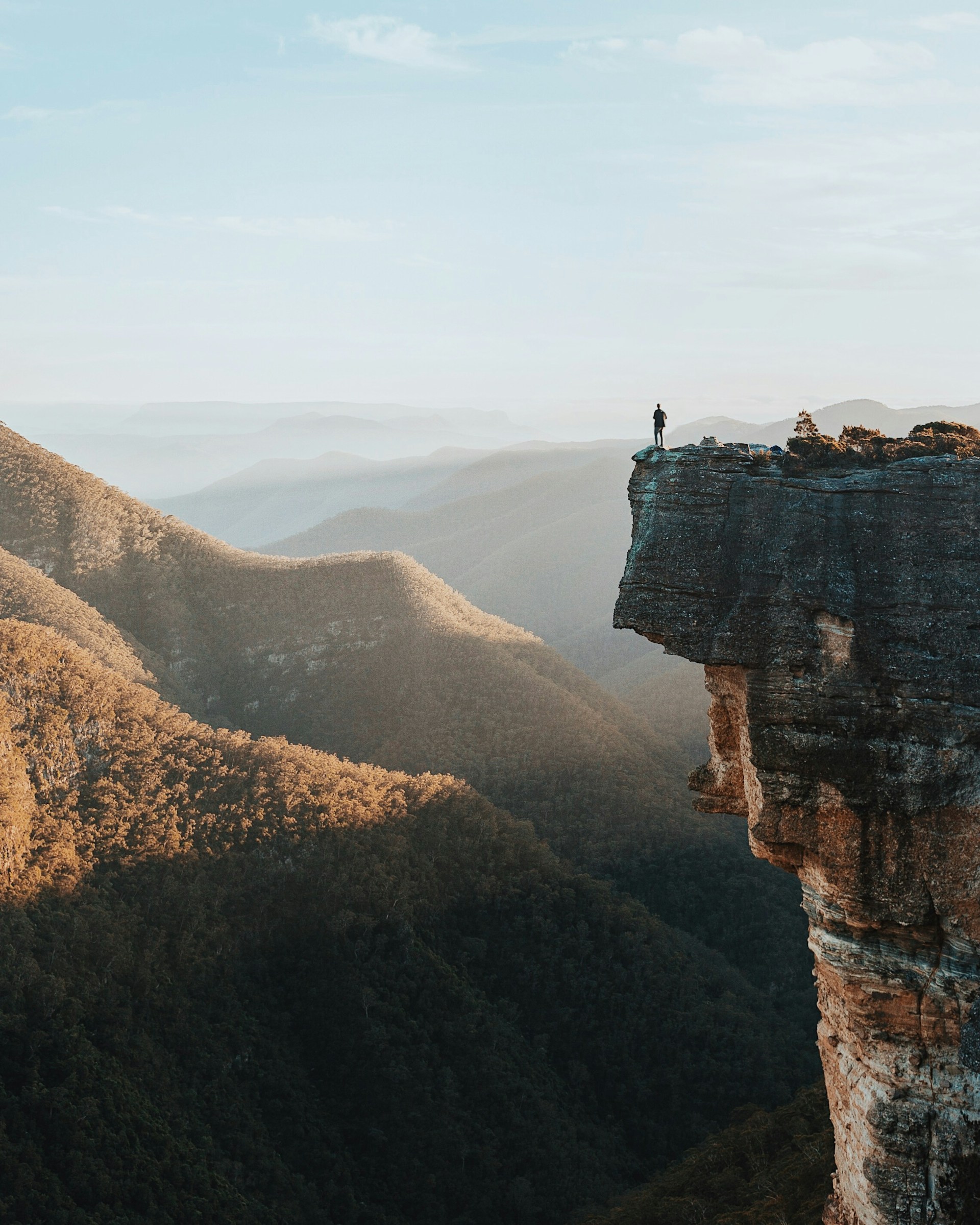 A man with a backpack stands on a tall mountain overlooking a beautiful landscape 