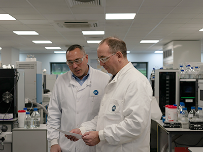 Scientist wearing purple gloves and safety glasses handling test tubes in a laboratory setting.