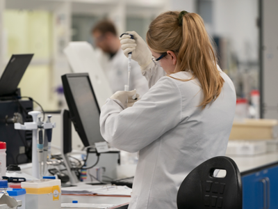 Scientists in white lab coats working with laboratory equipment in a bright, modern research lab.