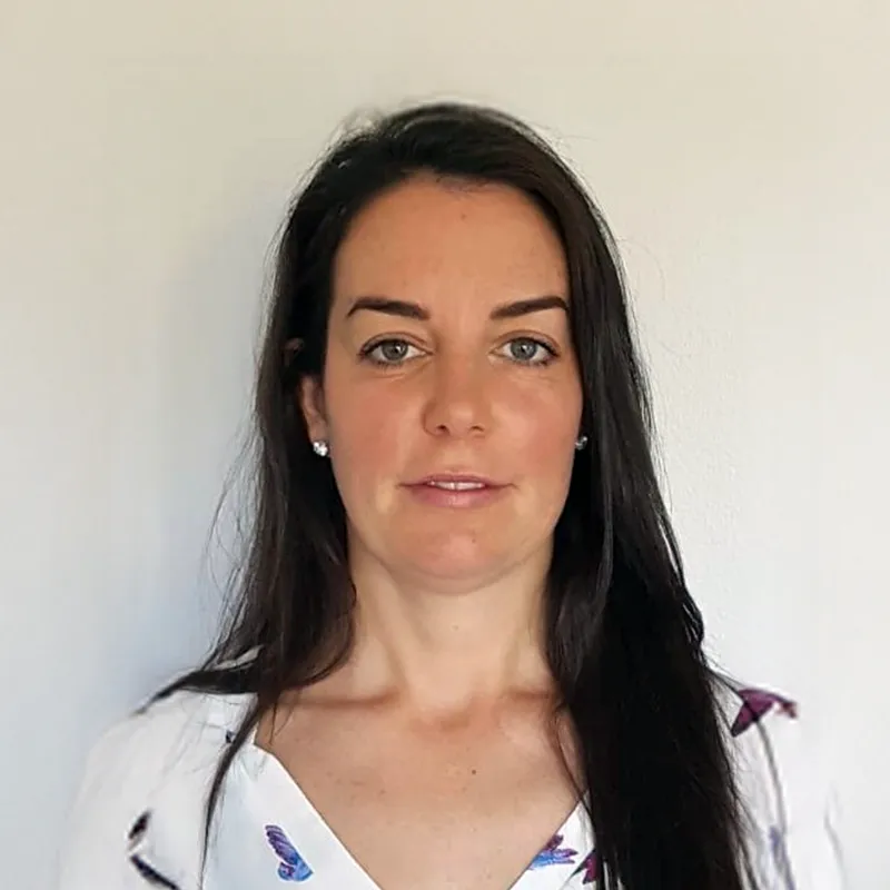 Portrait of a woman with long dark hair, wearing a white blouse with blue and purple butterfly prints, against a plain light background.